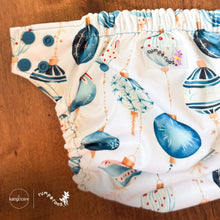 Load image into Gallery viewer, Rumparooz G3 One Size Pocket Cloth Diaper in Christmas print called Glaskugeln with blue and red ornament pattern on a white background, folded in half and laying on a table