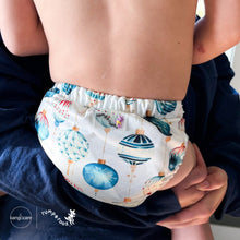 Load image into Gallery viewer, Baby in parents arms wearing a Rumparooz G3 One Size Pocket Cloth Diaper in Christmas print called Glaskugeln with blue and red ornament pattern on a white background