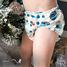 Load image into Gallery viewer, Baby standing at a Christmas tree wearing a Rumparooz G3 One Size Pocket Cloth Diaper in Christmas print called Glaskugeln with blue and red ornament pattern on a white background showing blue snaps