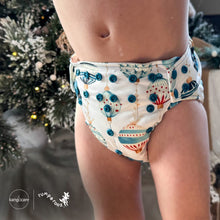 Load image into Gallery viewer, Baby standing at a Christmas tree wearing a Rumparooz G3 One Size Pocket Cloth Diaper in Christmas print called Glaskugeln with blue and red ornament pattern on a white background showing blue snaps