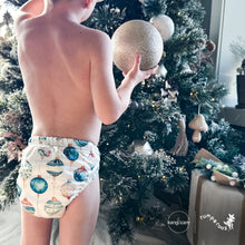 Load image into Gallery viewer, Baby standing at a Christmas tree wearing a Rumparooz G3 One Size Pocket Cloth Diaper in Christmas print called Glaskugeln with blue and red ornament pattern on a white background