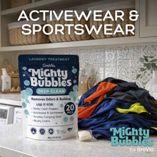 Load image into Gallery viewer, Mighty Bubbles laundry treatment packaging with a pile of colorful clothes on a kitchen counter.