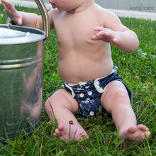 Load image into Gallery viewer, Young toddler sitting in the grass wearing a Shine Bright Newborn Cover, facing the camera

