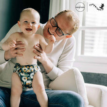 Load image into Gallery viewer, Man holding a baby wearing a dandelion cloth diaper, with 'Rumparooz' by Kanga Care branding visible.
