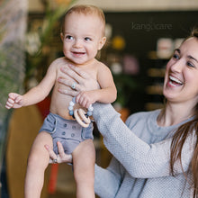 Load image into Gallery viewer, Baby in a Glacier Ecoposh OBV holding a Pebble Teething Ring