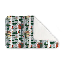 Load image into Gallery viewer, Kanga Care Changing Pad and Sheet Saver in the print called Evergreen with a winter village pattern, featuring small houses, evergreen trees, and red accents on a light gray background, with a white plush backing shown on the curled corner.
