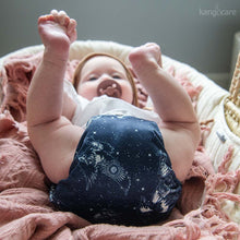 Load image into Gallery viewer, Baby laying on their back in a basinet, holding their toes and wearing a Shine Bright Rumparooz OBV
