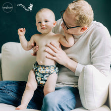 Load image into Gallery viewer, Man holding a baby wearing a dandelion cloth diaper, with 'Rumparooz' by Kanga Care branding visible.
