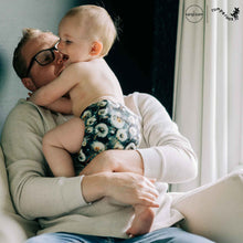 Load image into Gallery viewer, Man holding a baby wearing a dandelion cloth diaper, with 'Rumparooz' by Kanga Care branding visible.
